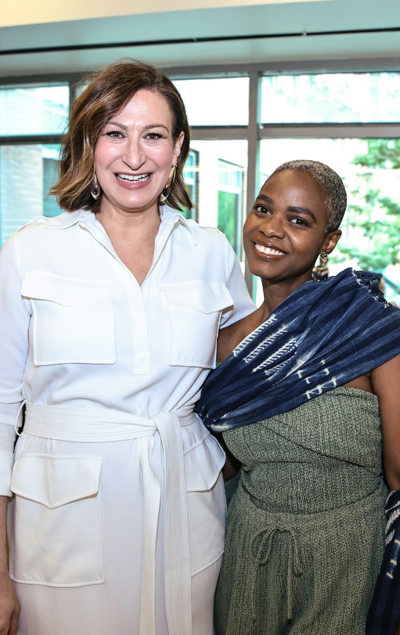 Two smiling women standing side by side in front of a bright window