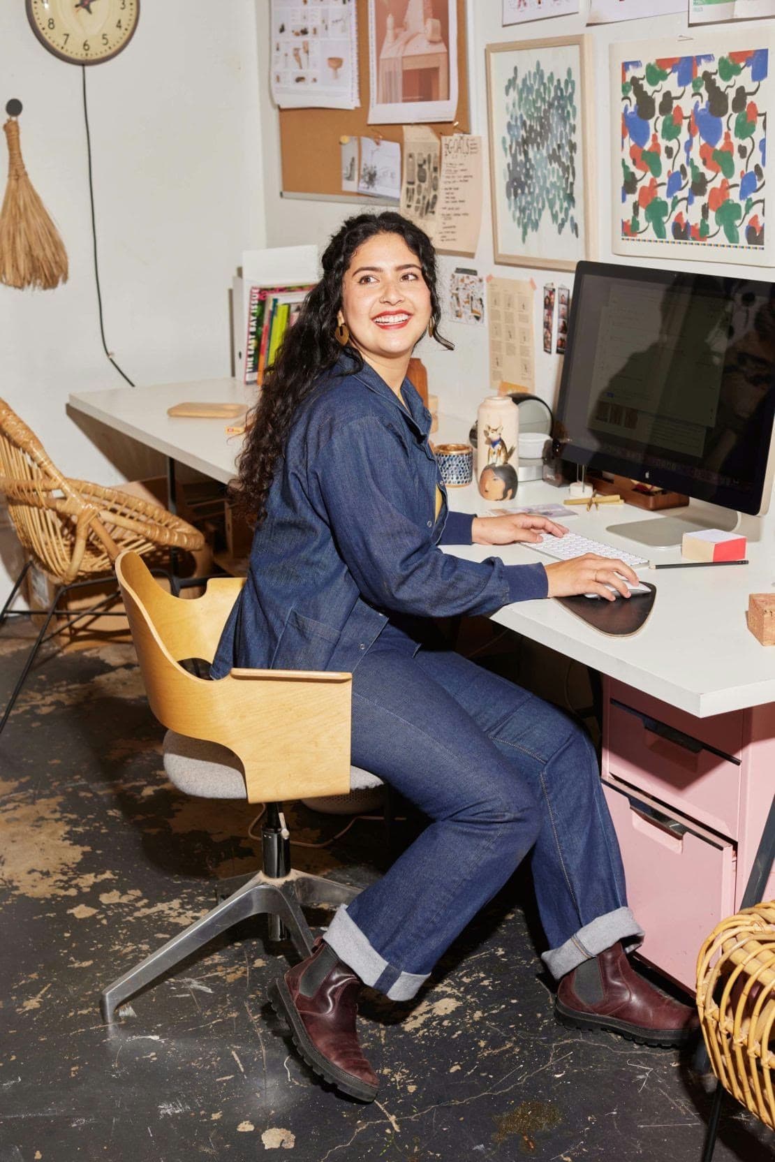A woman smiles over her shoulder while working at a desk in a creative studio